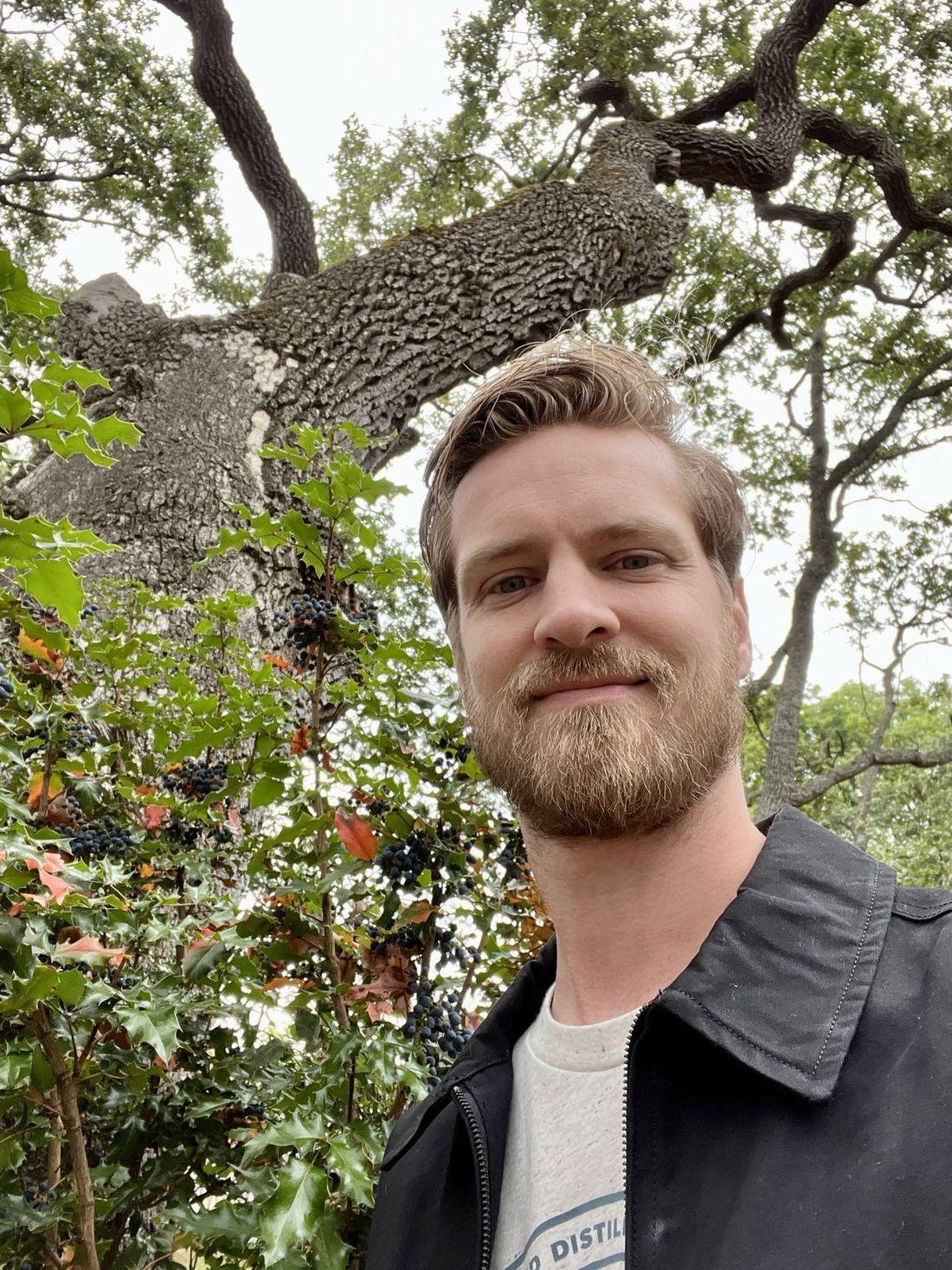 Tyler Pederson under a Garry oak, Quercus garryana, with Oregon grape in fruit beside him